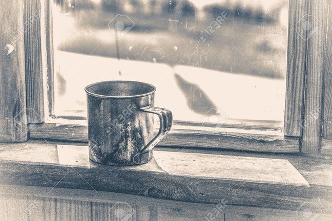 Old vintage photo. Old metal mug stands on a wooden window sill